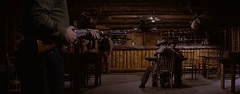 Movie still from “Jubal” (1956), directed by Delmer Daves – A man sitting on a chair in a room with a gun; Wide shot, Low angle