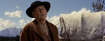 Movie still from “Jubal” (1956), directed by Delmer Daves – An old man wearing a cowboy hat standing in front of a covered wagon; Close Up shot, Low angle