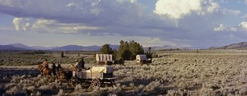 Movie still from “Jubal” (1956), directed by Delmer Daves – A man riding on the back of a covered wagon in a field; Extreme Wide shot, Low angle