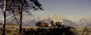 Movie still from “Jubal” (1956), directed by Delmer Daves – A group of people riding in a covered wagon on top of a grass covered hill; Wide shot, Low angle