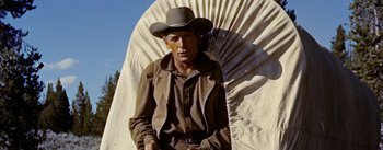 Movie still from “Jubal” (1956), directed by Delmer Daves – A man wearing a cowboy hat standing in front of an umbrella; Medium shot, Low angle