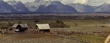 Movie still from “Jubal” (1956), directed by Delmer Daves – An old barn in the middle of a field with mountains in the background; Extreme Wide shot, High angle