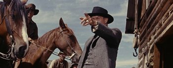 Movie still from “Jubal” (1956), directed by Delmer Daves – A man in a suit and a hat is holding a horse; Medium shot, Low angle