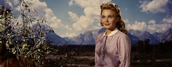 Movie still from “Jubal” (1956), directed by Delmer Daves – A woman in a purple dress standing in front of mountains; Medium shot, Low angle