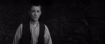 Movie still from “Jude” (1996), directed by Michael Winterbottom – A young man standing in front of a dark background; Medium shot, High angle