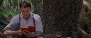 Movie still from “Jude” (1996), directed by Michael Winterbottom – A man sitting on the ground reading a book; Medium shot, Low angle