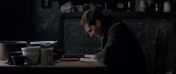 Movie still from “Jude” (1996), directed by Michael Winterbottom – A man sitting at a table reading a book in front of a fire place; Medium shot, High angle