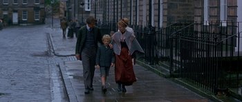 Movie still from “Jude” (1996), directed by Michael Winterbottom – A man , woman , and child walking down a sidewalk; Wide shot, High angle