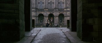 Movie still from “Jude” (1996), directed by Michael Winterbottom – Two people walking down a brick road in front of a building; Extreme Wide shot, High angle