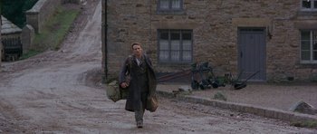 Movie still from “Jude” (1996), directed by Michael Winterbottom – A woman walking down a dirt road carrying luggage; Wide shot, High angle