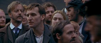 Movie still from “Jude” (1996), directed by Michael Winterbottom – A group of people standing next to each other; Close Up shot, Over the shoulder angle