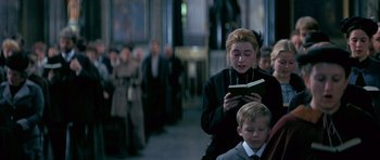 Movie still from “Jude” (1996), directed by Michael Winterbottom – A woman reading a book while standing next to a child; Medium shot, Over the shoulder angle