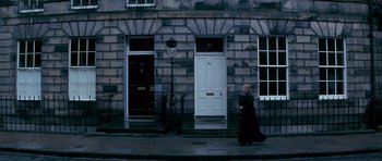 Movie still from “Jude” (1996), directed by Michael Winterbottom – A woman walking down the street in front of a building; Extreme Wide shot, High angle