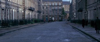Movie still from “Jude” (1996), directed by Michael Winterbottom – A group of people walking down a street near a building; Extreme Wide shot, High angle
