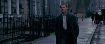 Movie still from “Jude” (1996), directed by Michael Winterbottom – A man wearing a trench coat walking down a sidewalk; Medium shot, Low angle
