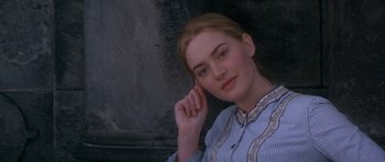 Movie still from “Jude” (1996), directed by Michael Winterbottom – A young woman posing for a picture in front of a stone wall; Close Up shot, Over the shoulder angle