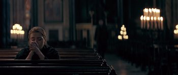 Movie still from “Jude” (1996), directed by Michael Winterbottom – A person sitting on a bench in front of candles; Medium shot, High angle