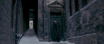 Movie still from “Jude” (1996), directed by Michael Winterbottom – A man standing in front of a door way; Wide shot, High angle