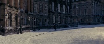 Movie still from “Jude” (1996), directed by Michael Winterbottom – A person walking down a snowy sidewalk near a building; Extreme Wide shot, High angle