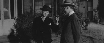 Movie still from “Jules and Jim” (1962), directed by François Truffaut – A man in a suit and a hat talking to another man in a suit and a hat; Medium shot, Over the shoulder angle