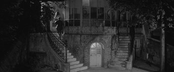 Movie still from “Jules and Jim” (1962), directed by François Truffaut – A woman walking up a set of stairs in front of a building; Extreme Wide shot, Low angle