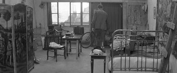 Movie still from “Jules and Jim” (1962), directed by François Truffaut – A man standing in a room holding a bicycle; Wide shot, High angle