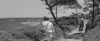 Movie still from “Jules and Jim” (1962), directed by François Truffaut – A man walking along a path near the ocean; Wide shot, High angle