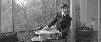 Movie still from “Jules and Jim” (1962), directed by François Truffaut – A man in a suit and hat holding a box; Medium shot, Low angle