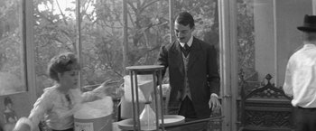 Movie still from “Jules and Jim” (1962), directed by François Truffaut – A black and white photo of a man standing in front of an hourglass; Medium shot, Low angle