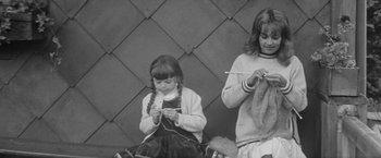 Movie still from “Jules and Jim” (1962), directed by François Truffaut – Two young girls are knitting while sitting on the ground; Medium shot, High angle