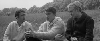 Movie still from “Jules and Jim” (1962), directed by François Truffaut – A man sitting next to another man in a field; Medium shot, Over the shoulder angle
