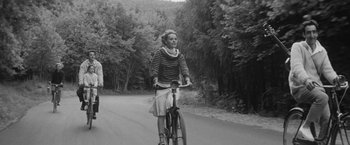 Movie still from “Jules and Jim” (1962), directed by François Truffaut – An older woman riding a bike down a road; Wide shot, High angle