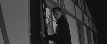 Movie still from “Jules and Jim” (1962), directed by François Truffaut – Black and white photograph of a young man looking out a window; Medium shot, Low angle