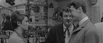 Movie still from “Jules and Jim” (1962), directed by François Truffaut – Two men standing in front of a wall full of beer bottles; Medium shot, Over the shoulder angle