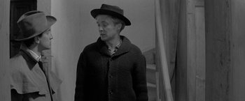 Movie still from “Jules and Jim” (1962), directed by François Truffaut – A man wearing a hat and a sweater standing in front of a staircase; Medium shot, Over the shoulder angle