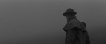Movie still from “Jules and Jim” (1962), directed by François Truffaut – A man wearing a hat and a coat standing in the fog; Medium shot, Over the shoulder angle