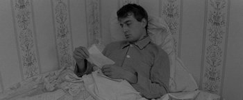 Movie still from “Jules and Jim” (1962), directed by François Truffaut – A man sitting in bed looking at a piece of paper; Medium shot, High angle
