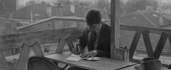 Movie still from “Jules and Jim” (1962), directed by François Truffaut – A man writing on a piece of paper on top of a wooden table; Medium shot, High angle