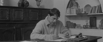 Movie still from “Jules and Jim” (1962), directed by François Truffaut – A man sitting at a table writing on a piece of paper; Medium shot, High angle