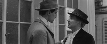 Movie still from “Jules and Jim” (1962), directed by François Truffaut – Two men in suits and hats talking to each other; Close Up shot, Over the shoulder angle