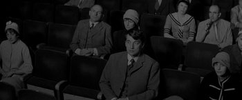 Movie still from “Jules and Jim” (1962), directed by François Truffaut – A man in a suit sitting next to two other people; Medium shot, High angle
