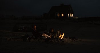 Movie still from “Julia” (1977), directed by Fred Zinnemann – A couple of people sitting on top of a sandy beach at night; Wide shot, Over the shoulder angle