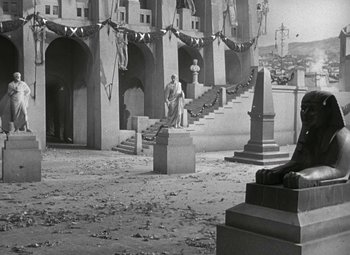 Movie still from “Julius Caesar” (1953), directed by Joseph L. Mankiewicz – An old photo of a man sitting on a bench in front of a building; Wide shot, High angle