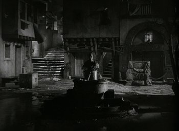 Movie still from “Julius Caesar” (1953), directed by Joseph L. Mankiewicz – A man sitting on a barrel in an abandoned building; Wide shot, High angle