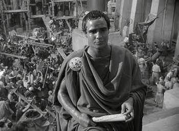 Movie still from “Julius Caesar” (1953), directed by Joseph L. Mankiewicz – A man in roman garb holding a book in front of a crowd of people; Medium shot, High angle