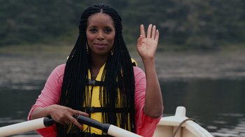 A woman in a pink and yellow jacket holding a paddle and waving