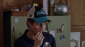 Movie still from “Junebug” (2005), directed by Phil Morrison – A young man wearing a panthers hat in front of a kitchen wall; Close Up shot, High angle