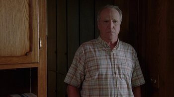 Movie still from “Junebug” (2005), directed by Phil Morrison – An older man standing in front of a wooden door; Medium shot, Over the shoulder angle