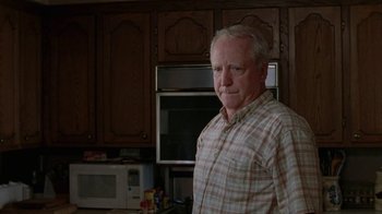 Movie still from “Junebug” (2005), directed by Phil Morrison – An older man standing in a kitchen next to an oven; Medium shot, Low angle
