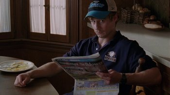 Movie still from “Junebug” (2005), directed by Phil Morrison – A man reading a newspaper while wearing a hat; Close Up shot, High angle